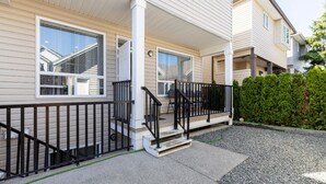 A two-story residential building with a covered porch, a small outdoor seating area, and a gravel driveway. - 3 bedroom spacious private basement suite (Langley)