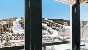 A view of a snow-covered ski resort with wooden chalets and a large building in the background. - Ski-in/out, mountain-view condo with hot tub, pool & gym (Big Sky)