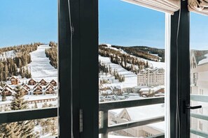 Blick auf einen verschneiten Skiort mit Holzhäusern und einem großen Gebäude im Hintergrund.