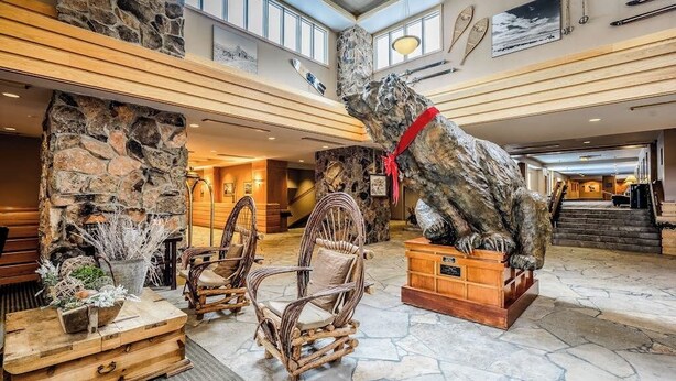 A lobby with stone walls, wicker chairs, a large bear statue, and a staircase. - Ski-in/out, mountain-view condo with hot tub, pool & gym (Big Sky)