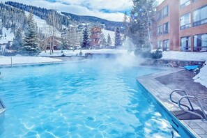 Ein Schwimmbecken mit klarem Wasser, umgeben von Gebäuden und schneebedeckten Bäumen.