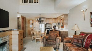 A spacious living area with a fireplace, a television, a sofa, and a dining table with chairs. - Ski-in/out, mountain-view condo with hot tub, pool & gym (Big Sky)