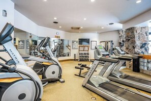 Ein Fitnessstudio mit Laufbändern, Kraftgeräten und einer Steinwand.