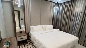 Habitación de hotel moderna con una cama grande, una mesita de noche con un libro, un espejo y una alfombra a rayas.