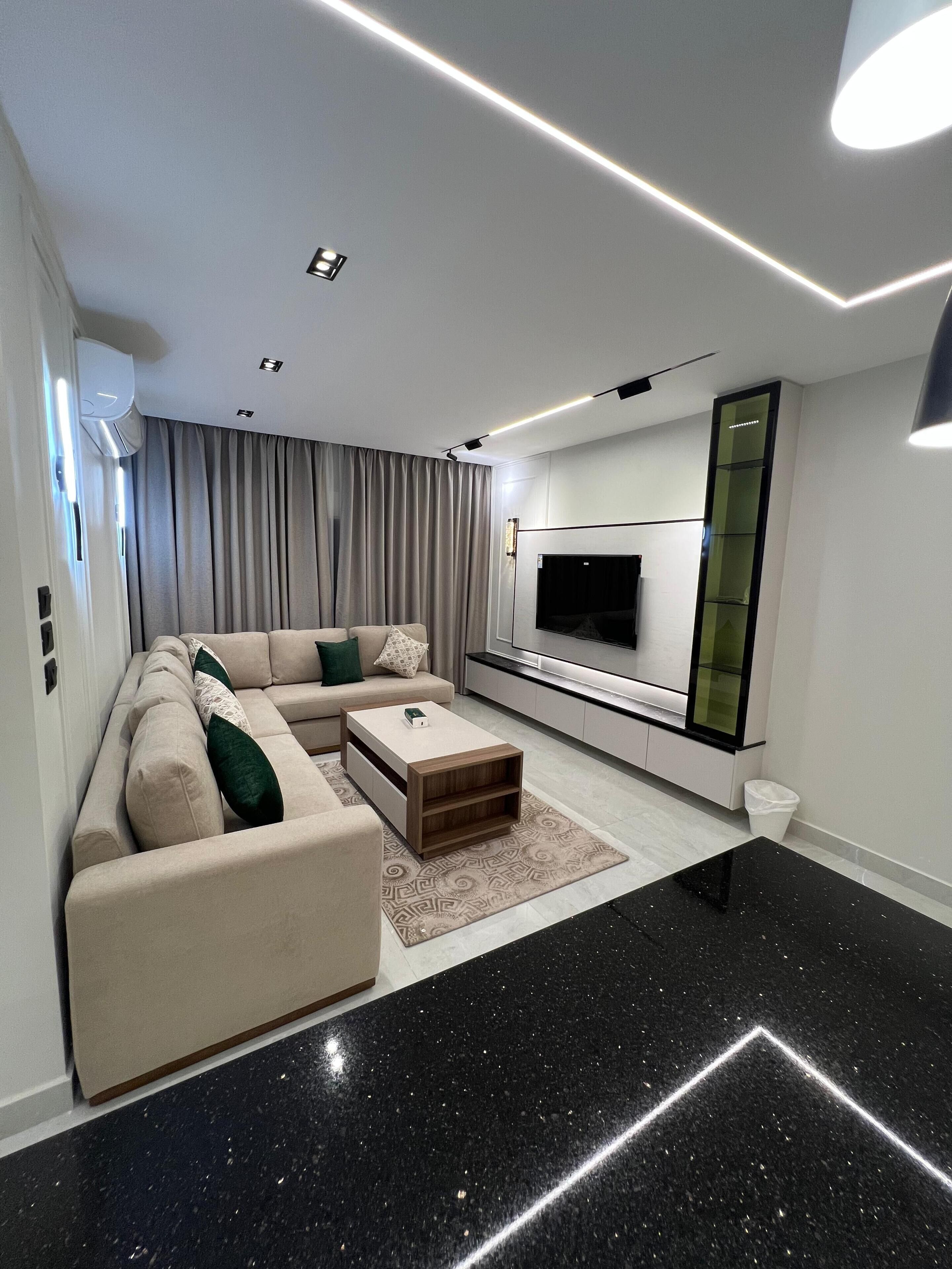 A modern living room with a sectional sofa, a coffee table, a flat-screen TV, and a minimalist design.