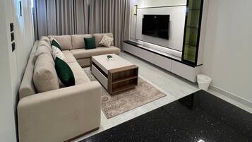 A modern living room with a sectional sofa, a coffee table, a flat-screen TV, and a minimalist design.