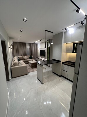 A modern kitchen with a central island, a dining area with a sofa, and a flat-screen TV mounted on the wall.