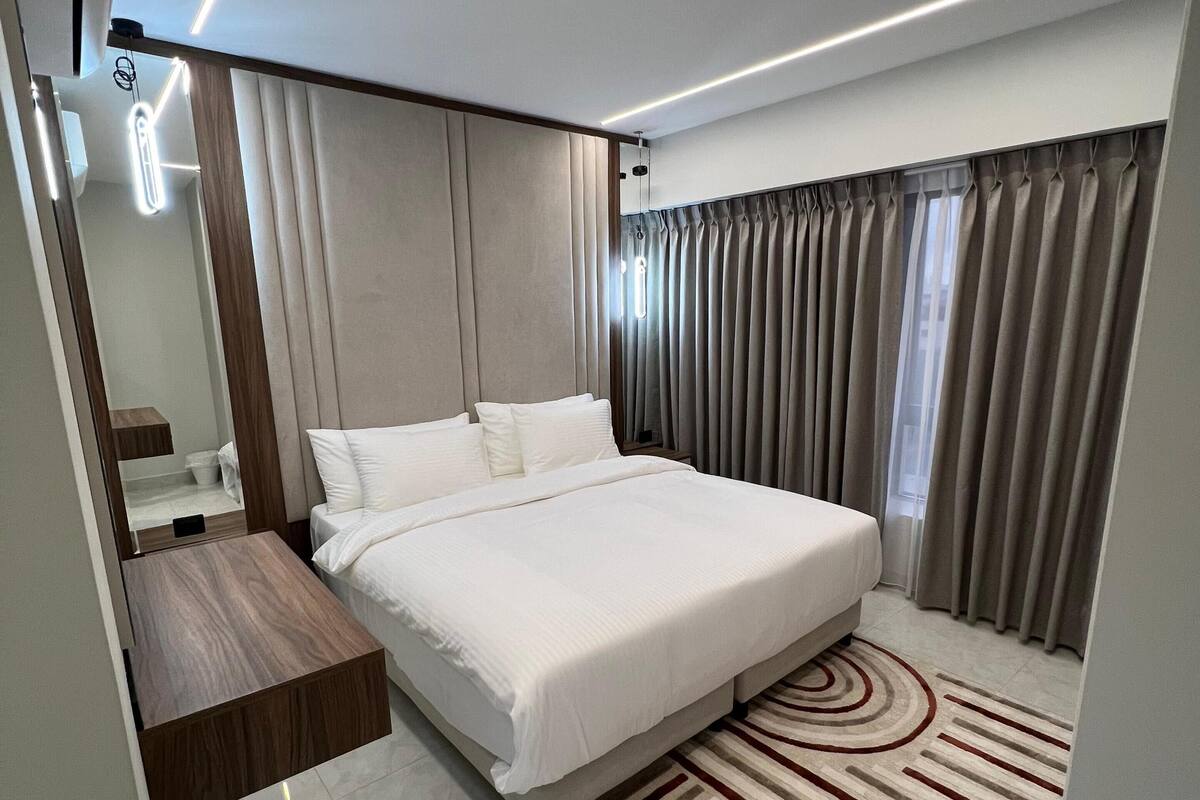 Una habitación de hotel moderna con una cama, una mesita de noche de madera, un espejo y una alfombra estampada.