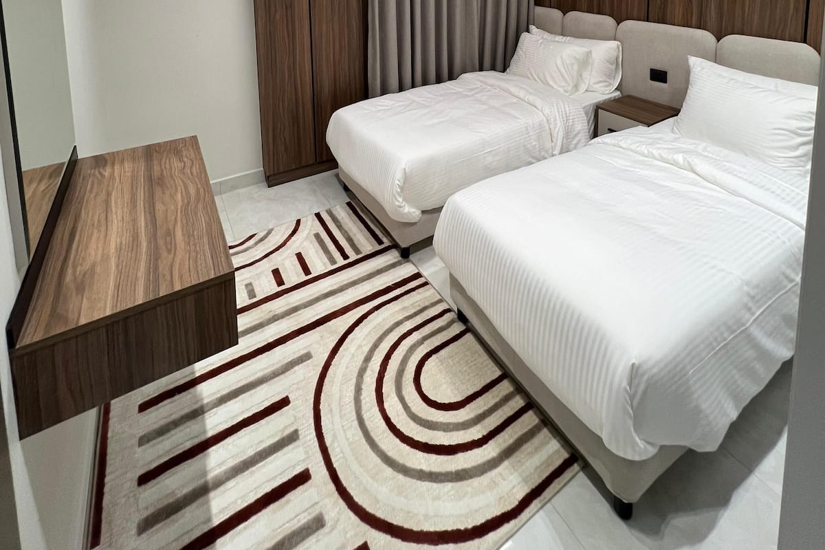 Una habitación de hotel moderna con dos camas, un escritorio de madera, un ventanal grande y un aire acondicionado instalado en el techo.