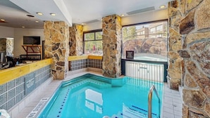 An indoor swimming pool with stone walls, a hot tub, and a poolside bar area. - Ski-in/ski-out ski chalet w/shared hot tub, pool, balcony, WiFi, central A/C (Big Sky)