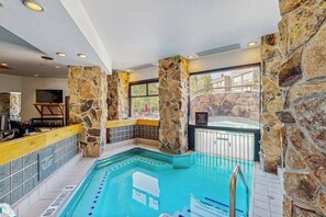 Een binnenzwembad met stenen muren, een jacuzzi en een barretje bij het zwembad.
