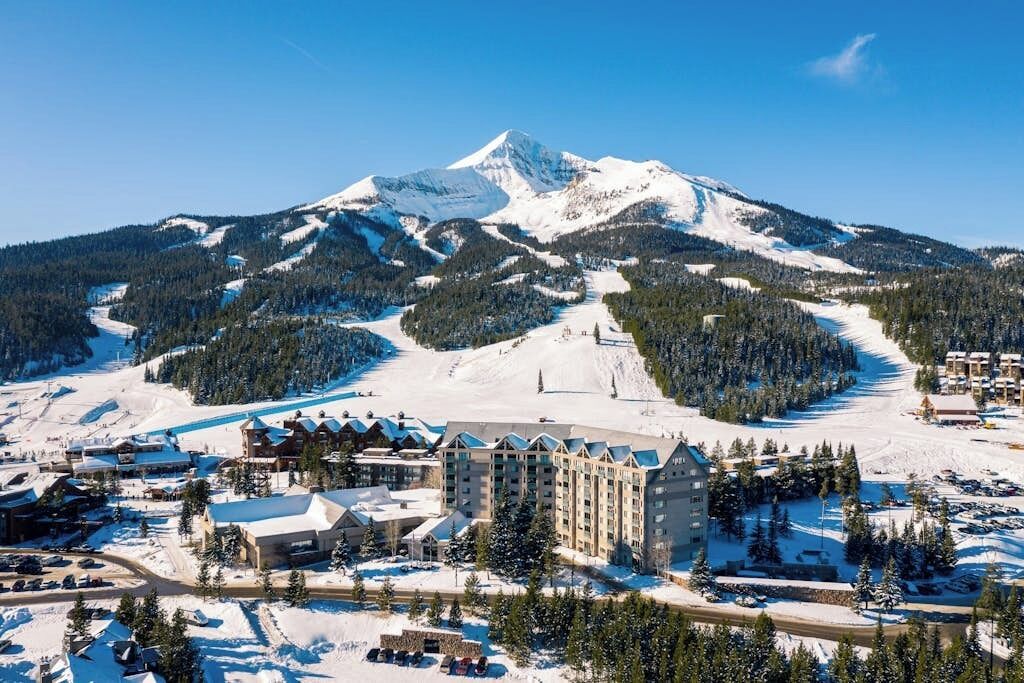 A snow-covered mountain with a ski resort, including a large building with multiple floors and a parking area.