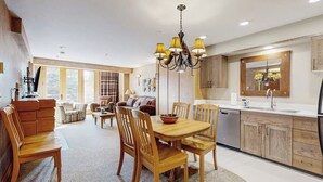A modern kitchen with wooden cabinets, a dining table, and chairs. - Ski-in/ski-out ski chalet w/shared hot tub, pool, balcony, WiFi, central A/C (Big Sky)