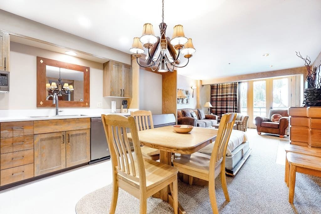 Een moderne keuken met houten kastjes, een eethoek met een houten tafel en stoelen, een kroonluchter, en een woonkamer met een bank en een open haard.