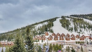 Un chalet comprenant plusieurs cabanes en bois, une piste de ski et un paysage montagneux boisé en arrière-plan.