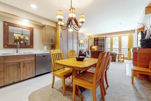 A modern kitchen with wooden cabinets, a dining table with chairs, and a chandelier. - Ski-in/ski-out condo in the village w/ shared pool/hot tub, sauna, gym & more (Big Sky)