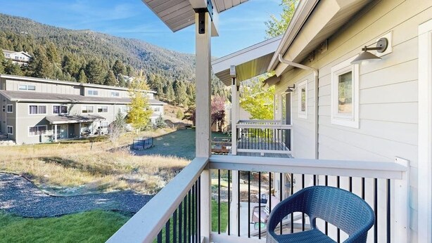 A balcony with a view of a river and houses, a chair, and a railing. - Immaculate Condo Near Meadow Village | New Carpet, Mountain Views & Dog-Friendly (Big Sky)