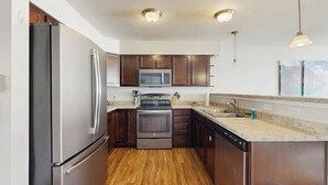 A modern kitchen with stainless steel appliances, wooden cabinets, and a granite countertop. - Immaculate Condo Near Meadow Village | New Carpet, Mountain Views & Dog-Friendly (Big Sky)