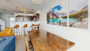 A dining area with a wooden table, chairs, and a large mountain landscape painting on the wall. - Immaculate Condo Near Meadow Village | New Carpet, Mountain Views & Dog-Friendly (Big Sky)