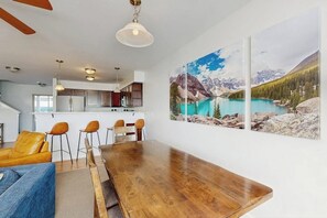 A dining area with a wooden table, chairs, and a large mountain landscape painting on the wall. - Immaculate Condo Near Meadow Village | New Carpet, Mountain Views & Dog-Friendly (Big Sky)