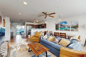 Ein modernes Wohnzimmer mit einer Couch, einem Couchtisch und Sesseln, eine Küche im Hintergrund sowie ein Essbereich mit Tisch und Stühlen.