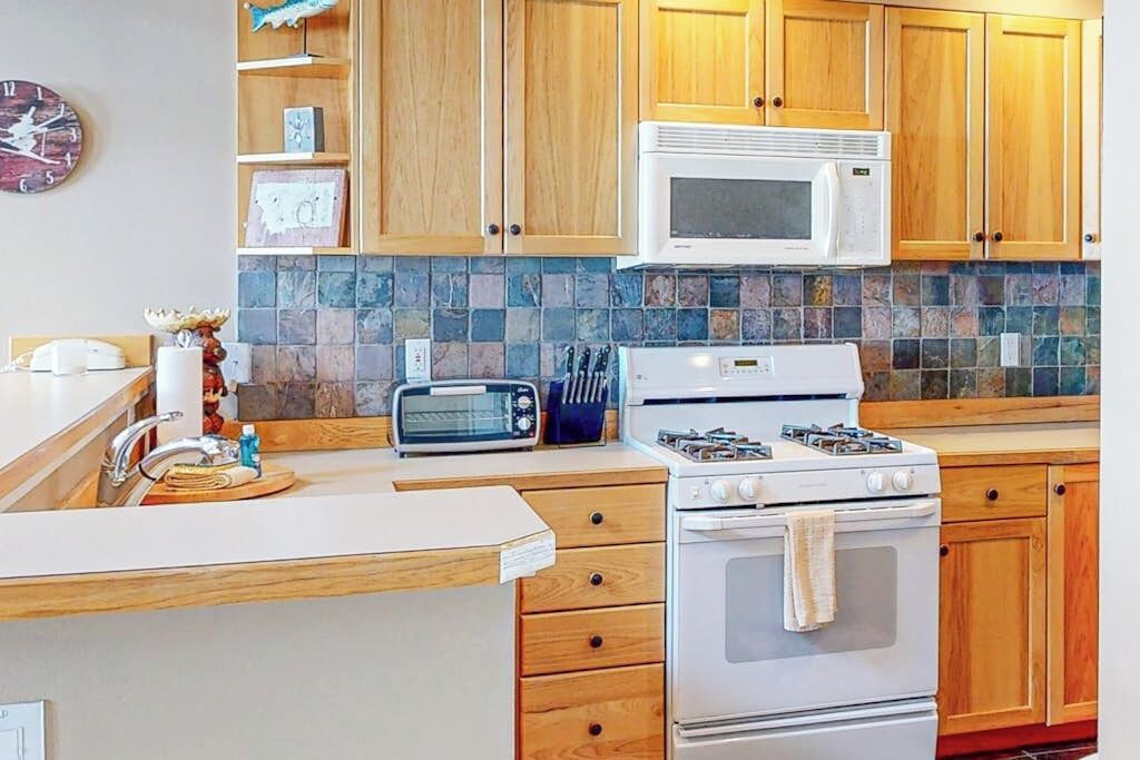 A kitchen with wooden cabinets, a microwave, a toaster, a stove, and a tiled backsplash.