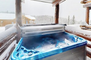 Una vasca idromassaggio in una baita di legno con vista su un paesaggio innevato.