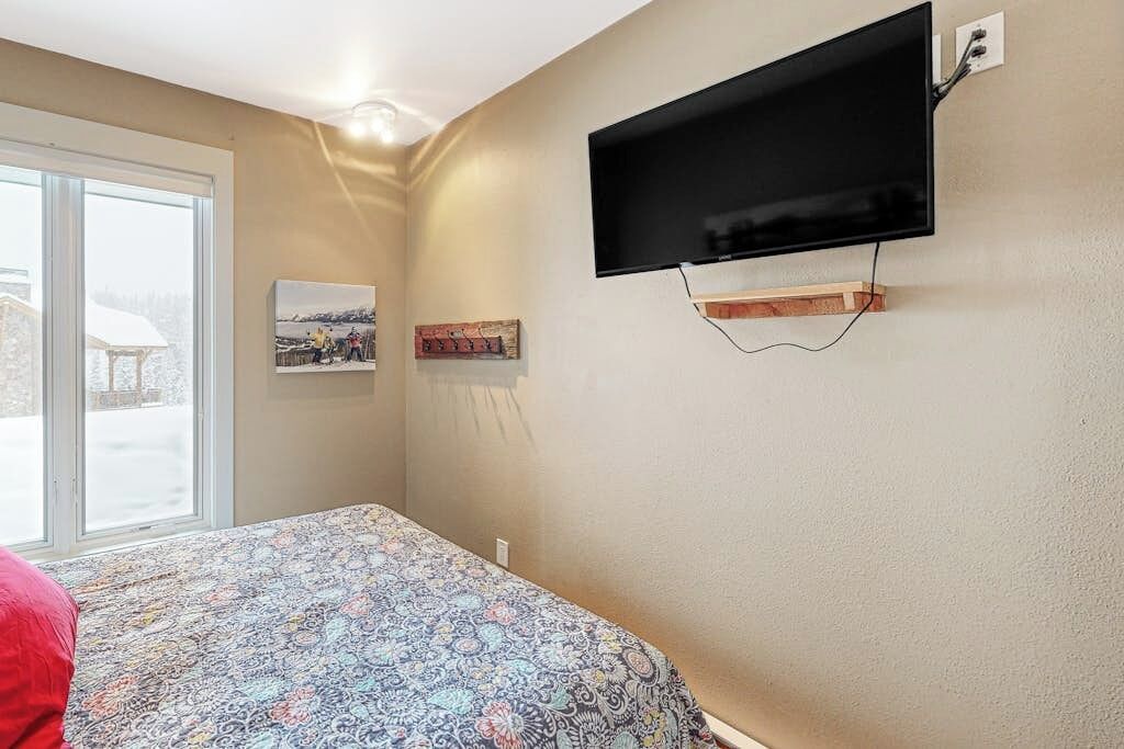 A bedroom with a bed, a mounted TV, and a window with a view of a snowy landscape.
