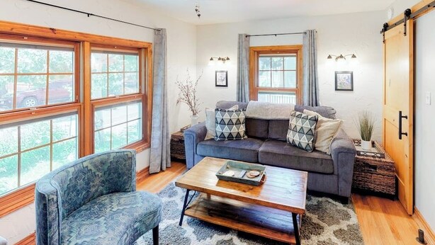 A living room with a sofa, a chair, a coffee table, and large windows. - Modern duplex with gas fireplace, free WiFi, & walkable downtown location (Bozeman)