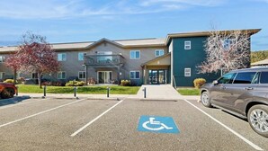 Un parking avec une place réservée aux personnes handicapées, un immeuble doté d’un balcon et une voiture garée devant.