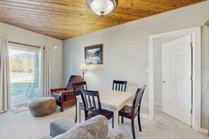 Ein Zimmer mit Holzboden, einem Esstisch mit Stühlen, einer Lampe, einem gerahmten Bild an der Wand und einer Tür.