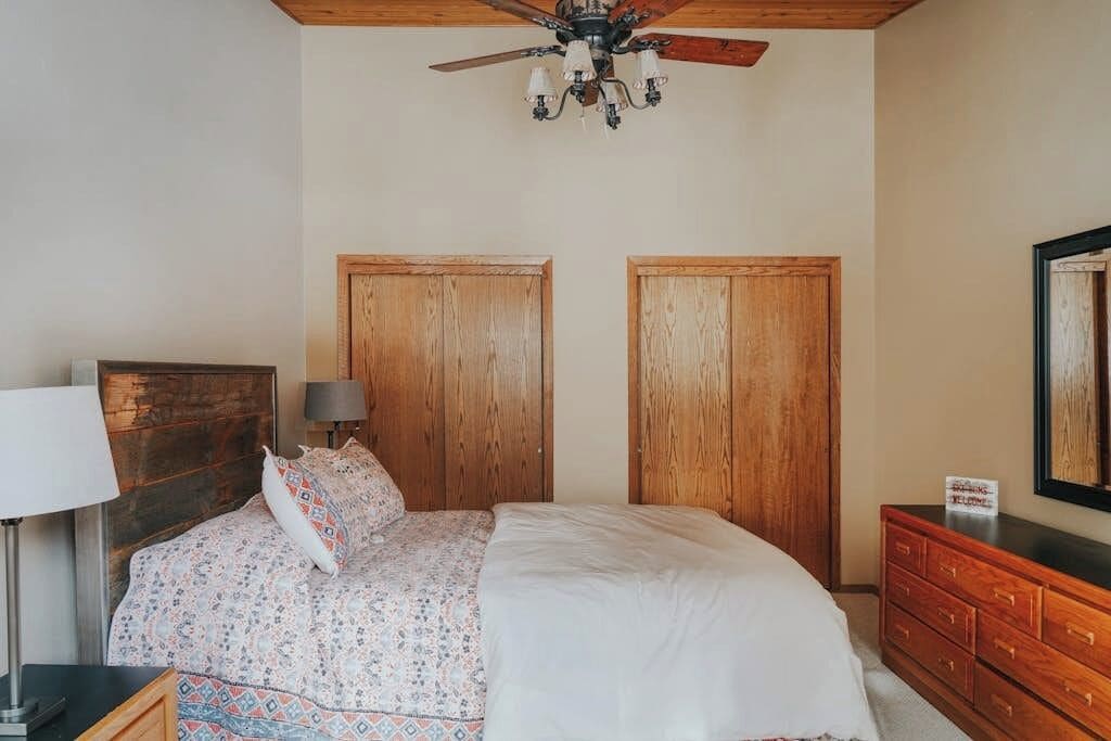 Ein Schlafzimmer mit Bett, Holzschrank, Schminktisch und Deckenventilator, sowie einer Kristallleuchter.