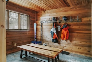 Ein Holzblockhaus-Innenraum mit einer Bank, Skiausrüstung und einem Fenster.