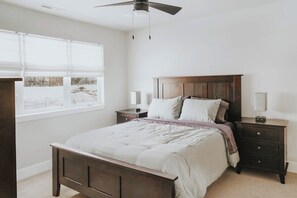 A bedroom with a bed, nightstands, a ceiling fan, and a window with blinds.