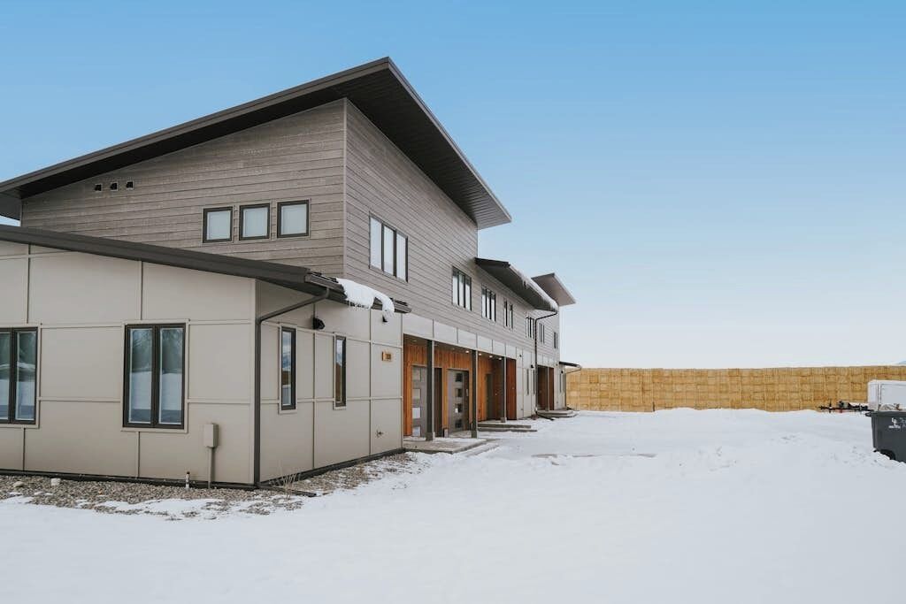 Un edificio de dos pisos con techo plano, ventanas amplias y suelo cubierto de nieve.