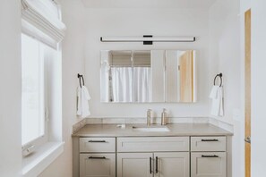 A bathroom with a window, a mirror, a sink, and cabinets.