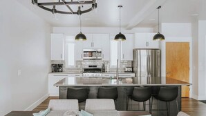 A modern kitchen with white cabinets, a central island, and black bar stools. - Beautiful home near ski resorts with patio, grill, washer/dryer, fast WiFi & AC (Bozeman)