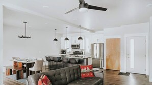 A modern living room with a sofa, dining area, kitchen, and a ceiling fan. - Beautiful home near ski resorts with patio, grill, washer/dryer, fast WiFi & AC (Bozeman)