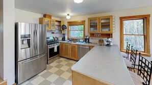 Een moderne keuken met roestvrijstalen apparatuur, houten kasten, een groot eiland en uitzicht op de omgeving door ramen.