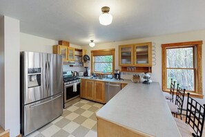 A modern kitchen with stainless steel appliances, wooden cabinets, a large island, and a view of the outdoors through windows. - Charming downtown retreat with stained glass, enclosed yard, and washer/dryer (Bozeman)