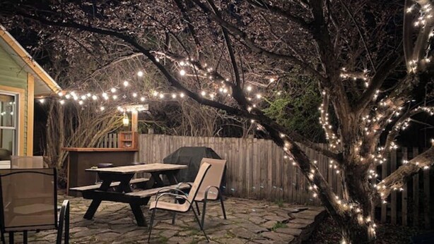 Een terras met een tafel en stoelen, een houten hek en een boom versierd met lichtjes.