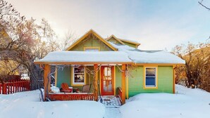 Een tweelaags huis met een groene gevel, een veranda met een rode deur en een sneeuwbedekt dak.