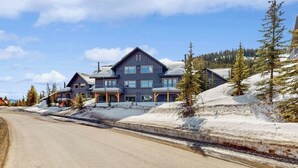 A large, multi-story building with a symmetrical design, located in a snowy landscape with a clear road in front. - Ski-in/out condo near Lake Levinsky with balcony, ski & mountain views (Big Sky)