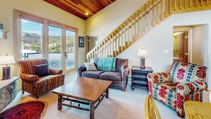 A spacious living area with a wooden ceiling, a staircase, and a view through large windows. - Ski-in/out condo near Lake Levinsky with balcony, ski & mountain views (Big Sky)