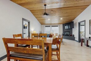 A dining area with a wooden table and chairs, a fireplace, and a modern kitchen in the background. - Fully Newly Remodeled Big Sky Condo with Mountain & Valley Views Private Hot Tub (Big Sky)