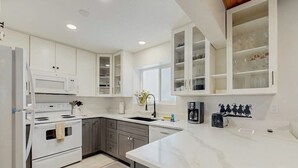 Une cuisine moderne avec des meubles blancs, un four à micro-ondes encastré, une cuisinière et une machine à café.