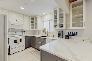 A modern kitchen with white cabinetry, a built-in microwave, a stove, and a coffee maker. - Fully Newly Remodeled Big Sky Condo with Mountain & Valley Views Private Hot Tub (Big Sky)