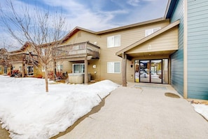 A two-story building with a covered entrance, a balcony, and a visible garage door. - Fully Newly Remodeled Big Sky Condo with Mountain & Valley Views Private Hot Tub (Big Sky)