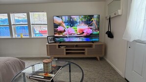 Una sala de estar con televisor, una mesa de vidrio, un sofá y una ventana con persianas.