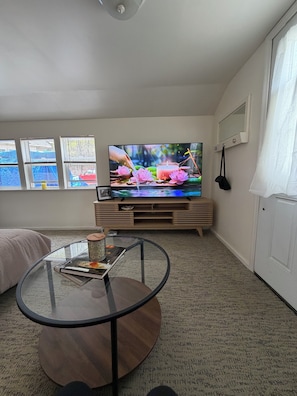 Een woonkamer met een televisie, een glazen tafel, een bank en een raam met jaloezieën.